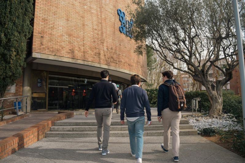 Estudiantes universitarios con mochilas caminando hacia la entrada de un edificio del campus para representar el acceso mediante identidad digital universitaria con EduID.