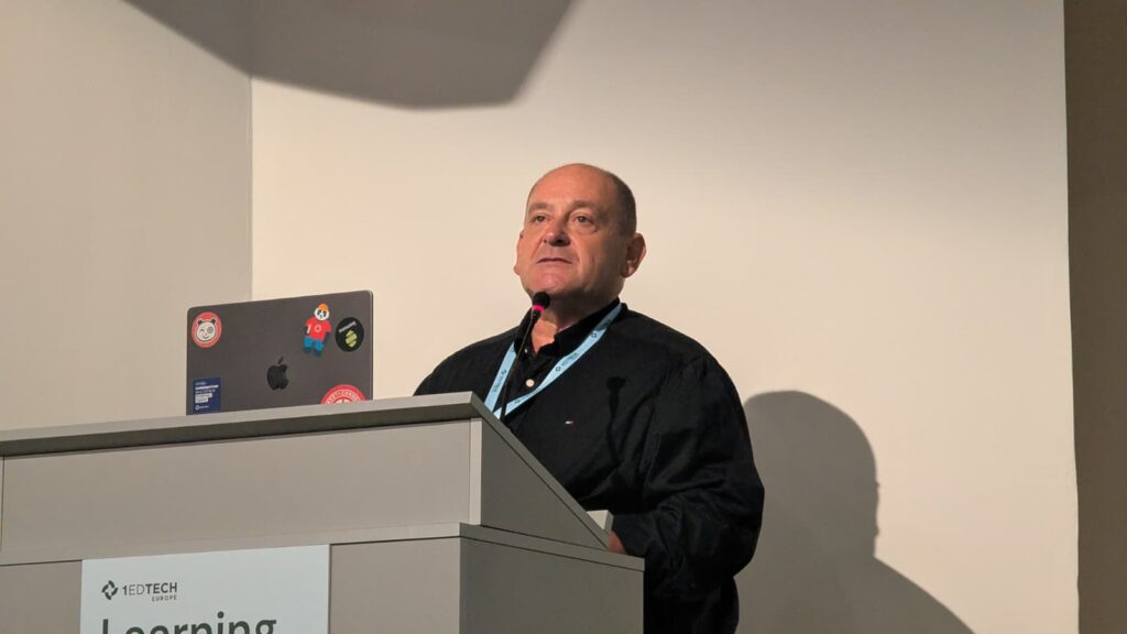 Speaker presenting at 1EdTech Learning Impact Europe conference with a laptop on stage